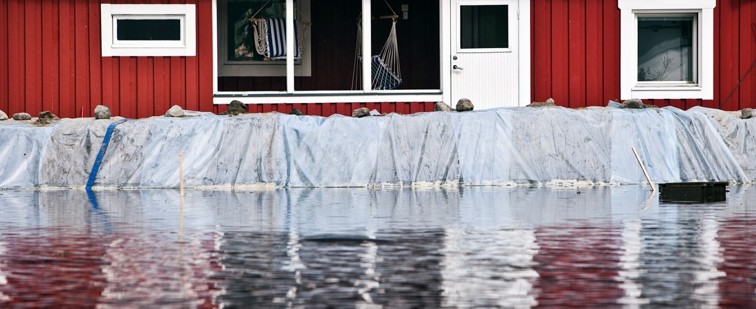 Översvämningsbarriärer framför rött översvämmat hus.