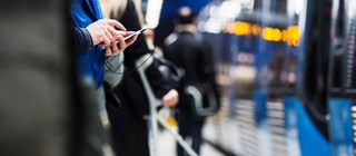 Människor som står och håller på med mobiltelefoner på en tunnelbaneperrong. 